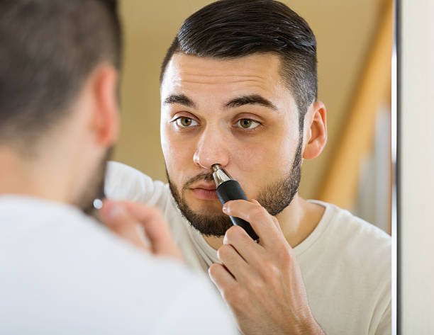 Man trimming nose hair with electric trimmer in front of mirror